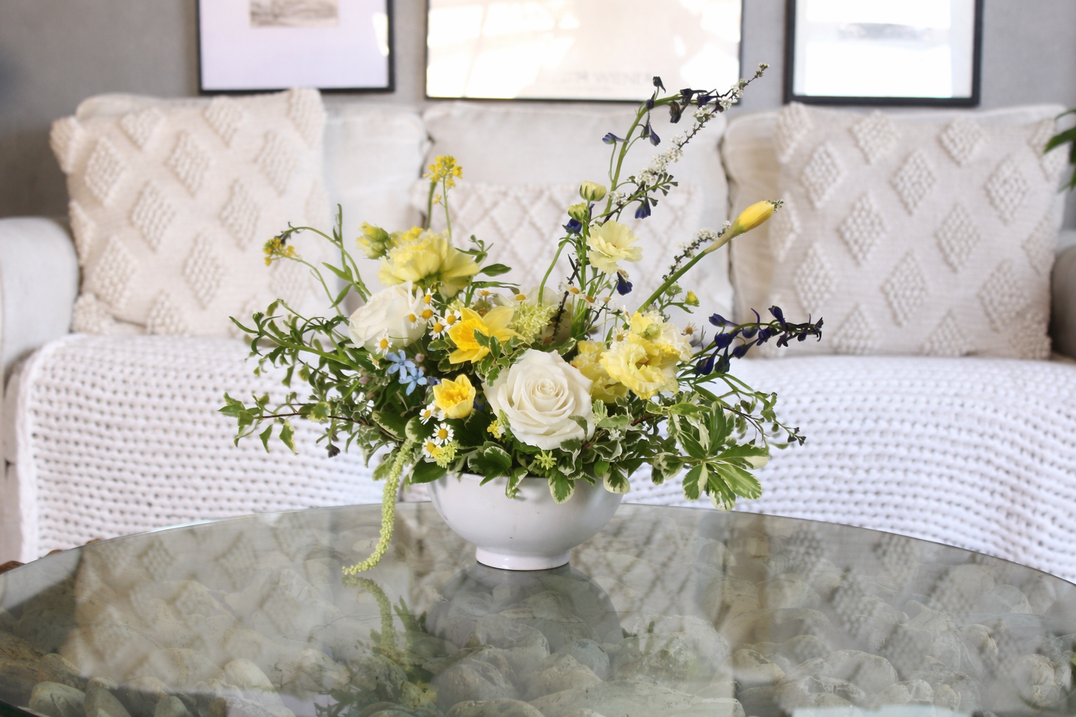 Buttercream and meadow-inspired floral arrangement with soft yellow, white, and blue blooms in a low ceramic vase.