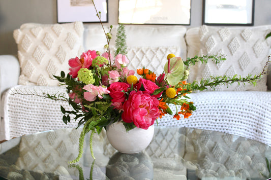 Bright floral arrangement with vibrant pink, yellow, and orange blooms in a modern ceramic vase. 