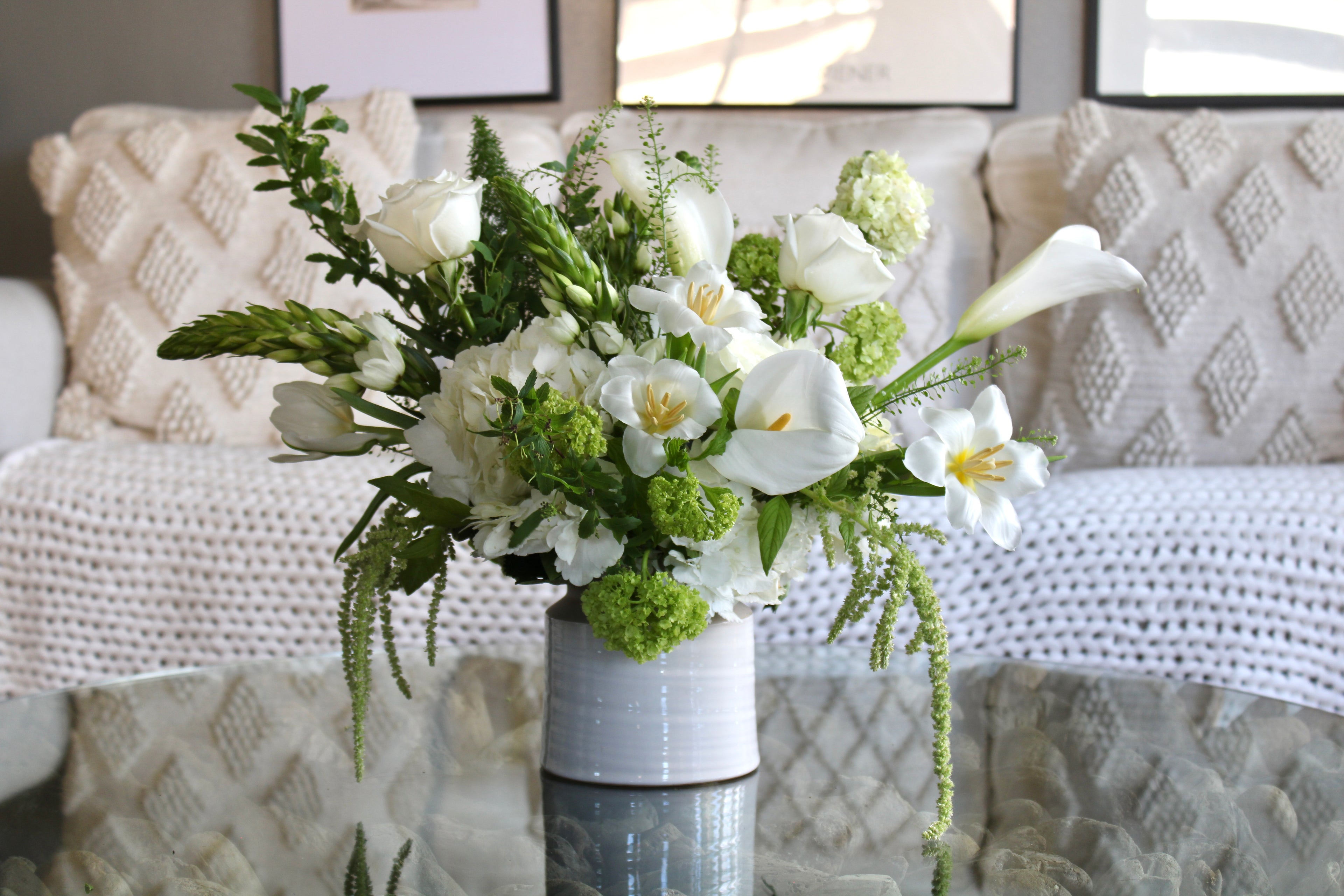 Ivory and green floral arrangement with white roses and seasonal greenery in ceramic vase.
