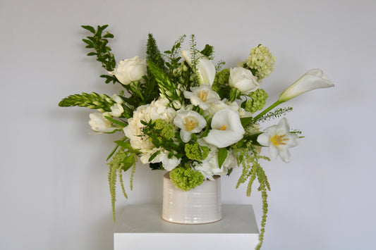 Ivory and green floral arrangement with white roses and seasonal greenery in ceramic vase.